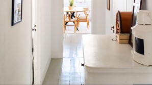 Un couloir aux murs blancs, orné de tableaux encadrés, avec une table en bois et un luminaire suspendu.