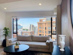 Een moderne woonkamer met een bank, een ronde salontafel en een groot raam met uitzicht op de stad.