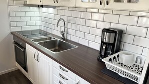 A kitchen with white cabinets, a double sink, a coffee maker, and a fruit basket.