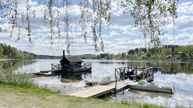 A lakeside dock with a small wooden structure, a boat, and a potted plant.