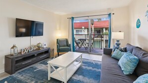 Ein Wohnzimmer mit Flachbildfernseher, einer Couch, einem Couchtisch, einem Fernsehmöbel und einem Balkon mit Tisch und Stühlen.
