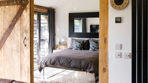 A bedroom with a large bed, a wooden door, a window with curtains, a wall clock, and a nightstand with a lamp. - Romantic Countryside Lodge With Hot Tub (Chichester)