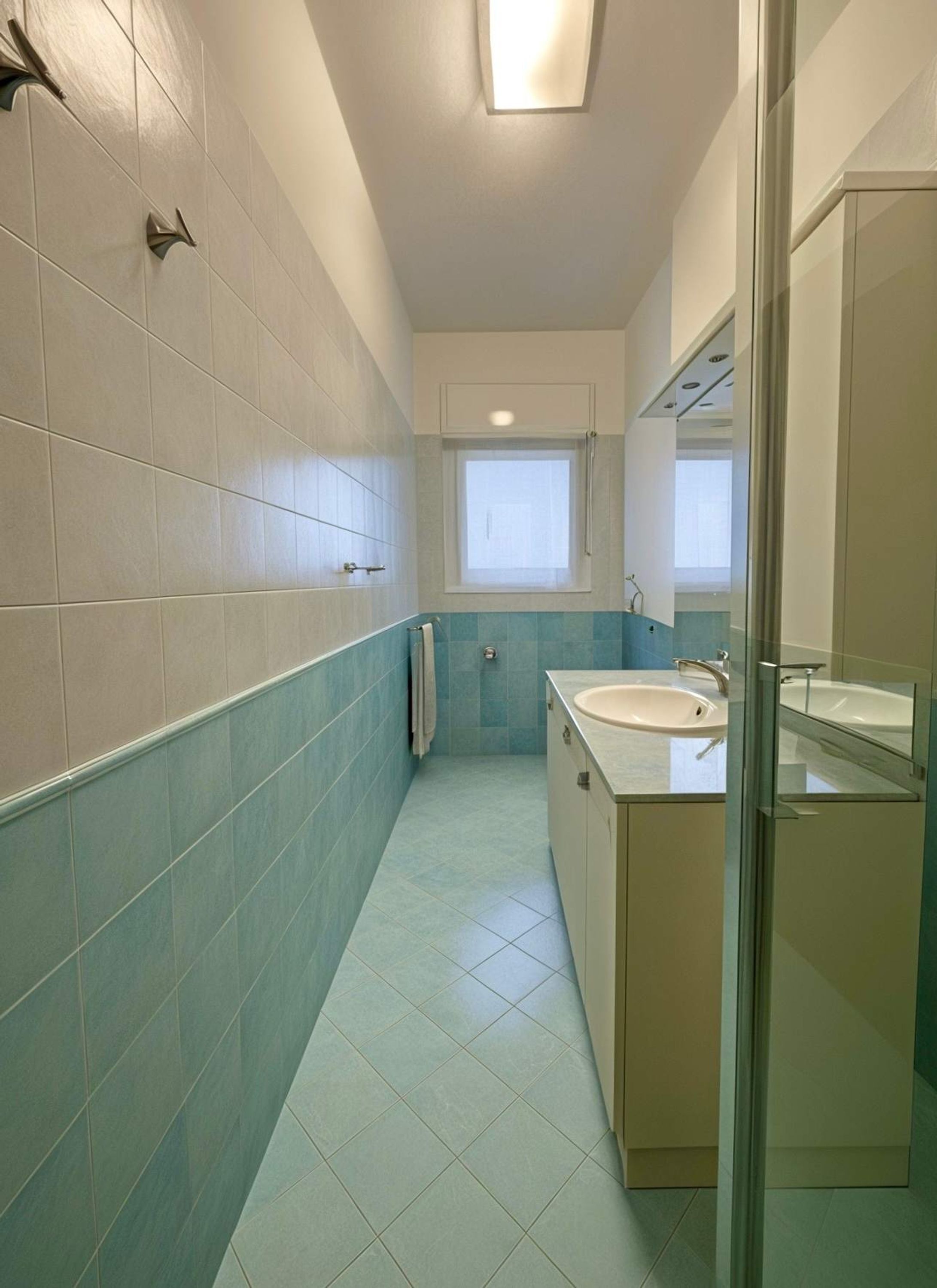 A narrow bathroom with a window, a sink, and a mirror.