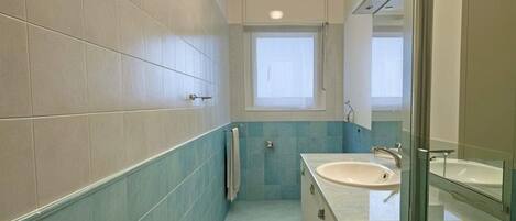 A narrow bathroom with a window, a sink, and a mirror.