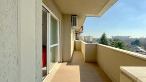 Ein schmaler Balkon mit Fliesenboden, einer Schiebeglastür und Blick auf entfernte Gebäude und Bäume.