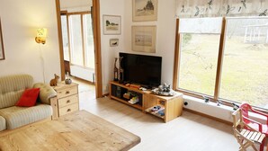 Una sala de estar con una mesa de madera, un sofá, un televisor y una ventana con vistas a un área verde.