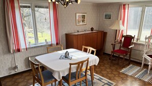 Comedor con una mesa dispuesta para cuatro, sillas de madera, un tapete estampado, un aparador de madera y una silla roja.