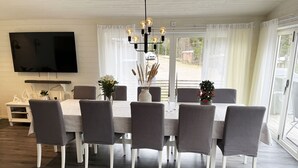 Een eetruimte met een tafel voor zes personen, omringd door stoelen, een aan de muur bevestigde televisie en uitzicht door grote ramen.