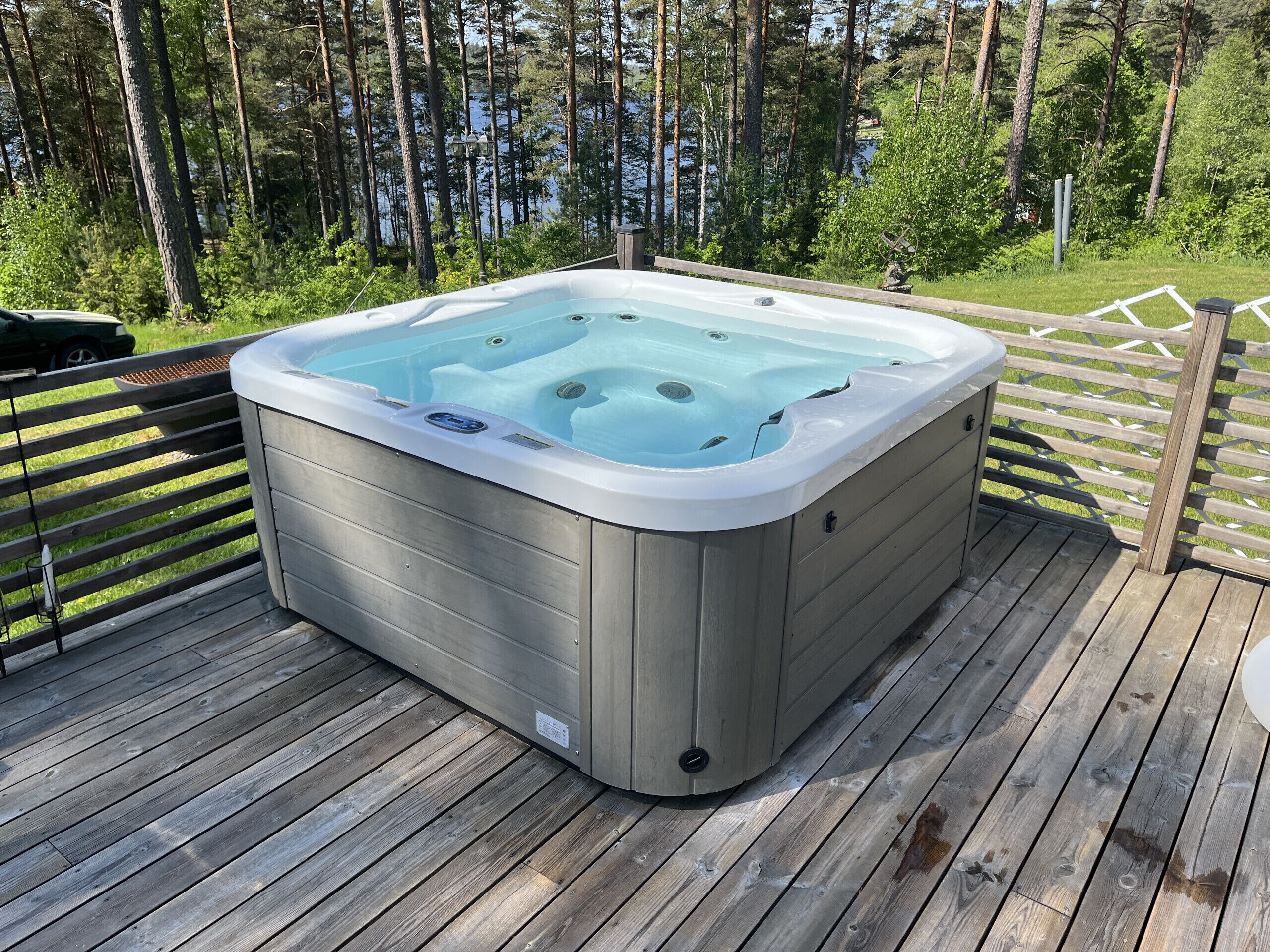 Un bain à remous sur une terrasse en bois, avec vue sur un lac et des arbres.