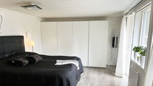 Een slaapkamer met een bed, een kledingkast, een radiator en een raam met planten.