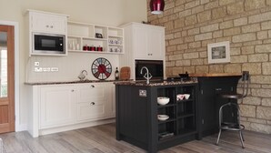 A kitchen with white cabinets, a black island, a microwave, a clock, and a brick wall.