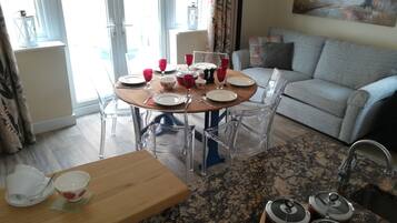 A dining area with a round table set for four, clear chairs, a wooden table, and a kitchen area with granite countertops and stainless steel appliances.