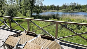 Una terraza de madera con sillas y barandilla, con vista a un lago rodeado de árboles.