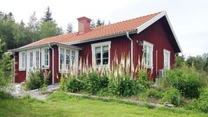 Una casa de madera roja con detalles blancos, una chimenea y un jardín con diversas plantas.