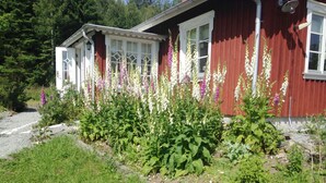 Un edificio rojo con detalles blancos, un camino de entrada de grava y un jardín con diversas plantas.