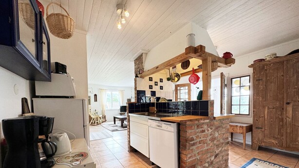 Una cocina con una isla de ladrillo, armarios blancos y un salpicadero de azulejos. Hay una zona de comedor con una mesa y sillas, y vistas al exterior a través de una ventana.