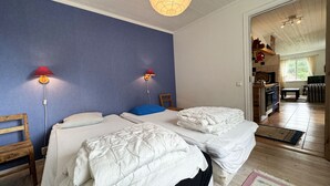 Una habitación con dos camas, piso de madera, pared azul y una cocina al fondo.