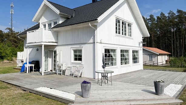 A white two-story house with a large deck, outdoor furniture, and a satellite dish.