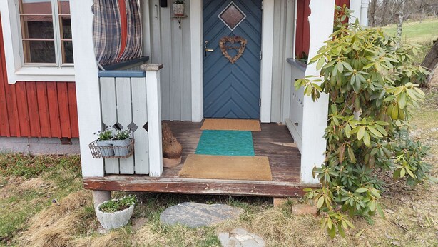 A wooden house with a blue door, a porch with a bench, and a small garden area.