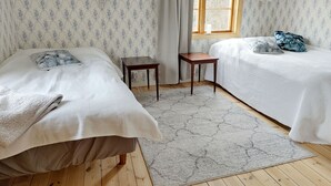 A room with two beds, a small table, a window, and patterned wallpaper.