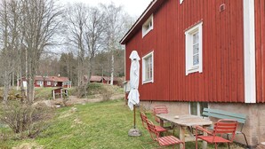 A red building with a table and chairs outside, a white umbrella, and a stone wall.