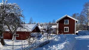 A red wooden house with a snow-covered roof, a clear blue sky, and a snow-covered ground.
