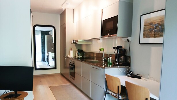 A modern kitchen with stainless steel appliances, a dining area with a wooden table and chairs, and a large window providing natural light. - Modern apartment in the center of Visby | SE12053 (Visby)
