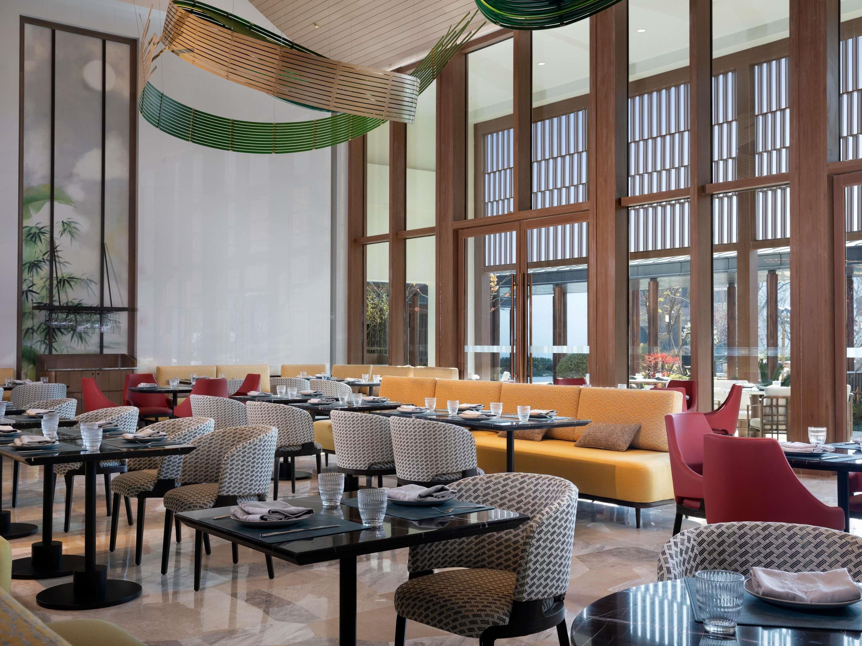 A modern dining area with multiple tables and chairs, large windows, and a ceiling with a unique light fixture.