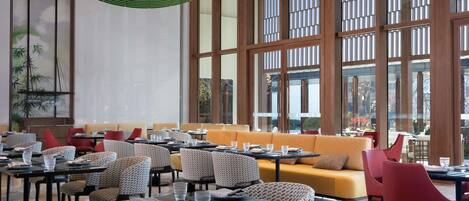 A modern dining area with multiple tables and chairs, large windows, and a ceiling with a unique light fixture.