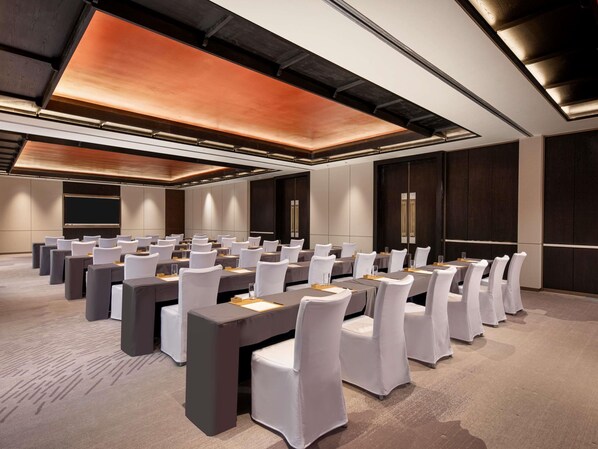 A conference room with rows of tables and chairs, a large screen, and a modern ceiling design.