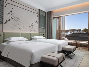 Quarto de hotel com duas camas, área de estar e uma grande janela com vista.