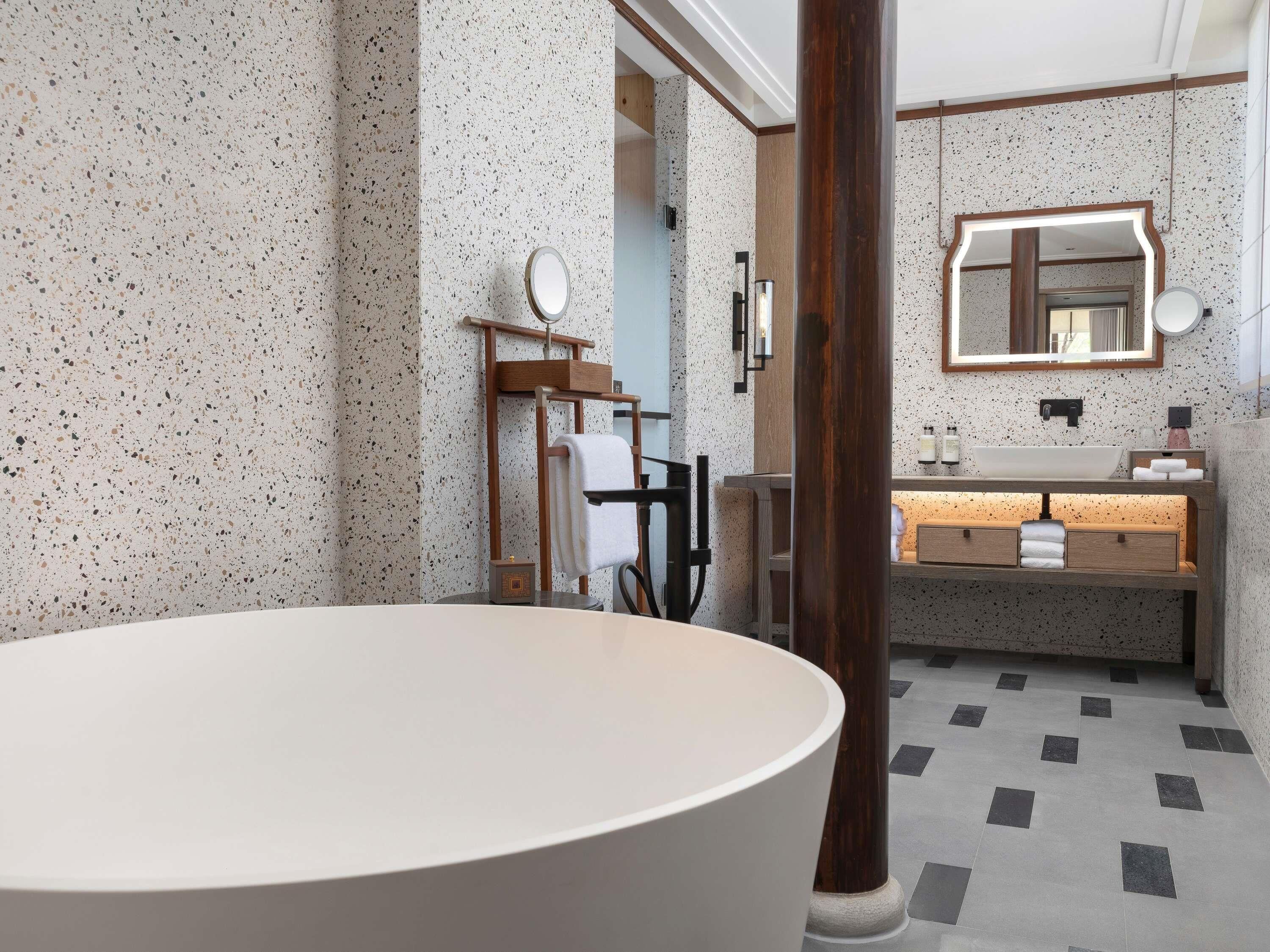 Ein modernes Badezimmer mit einer freistehenden Badewanne, einem hölzernen Waschtisch mit Spiegel und einer Wandgestaltung mit Farbflecken.