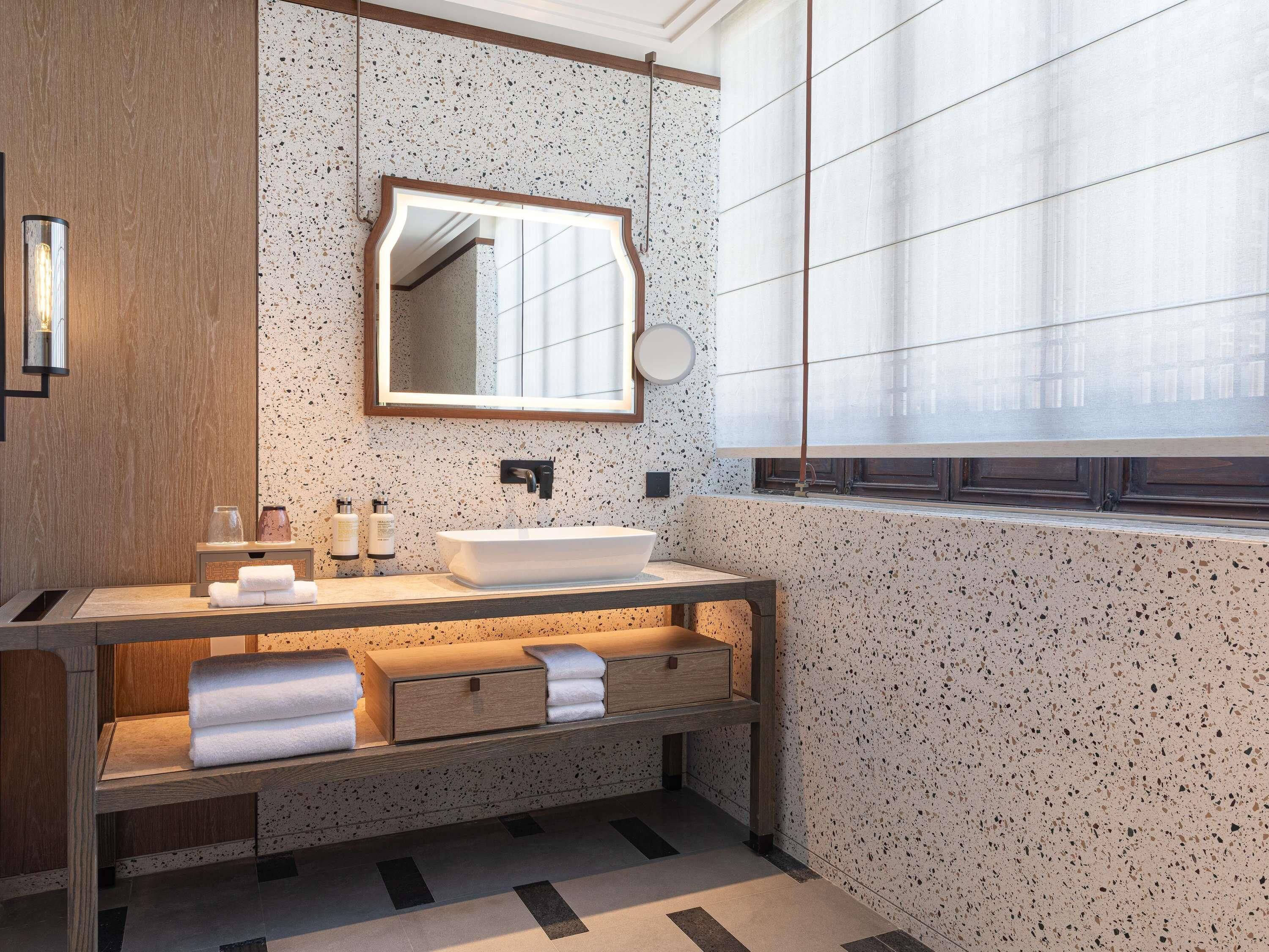 Un baño moderno con un lavamanos independiente, un espejo grande y una ventana con persianas.