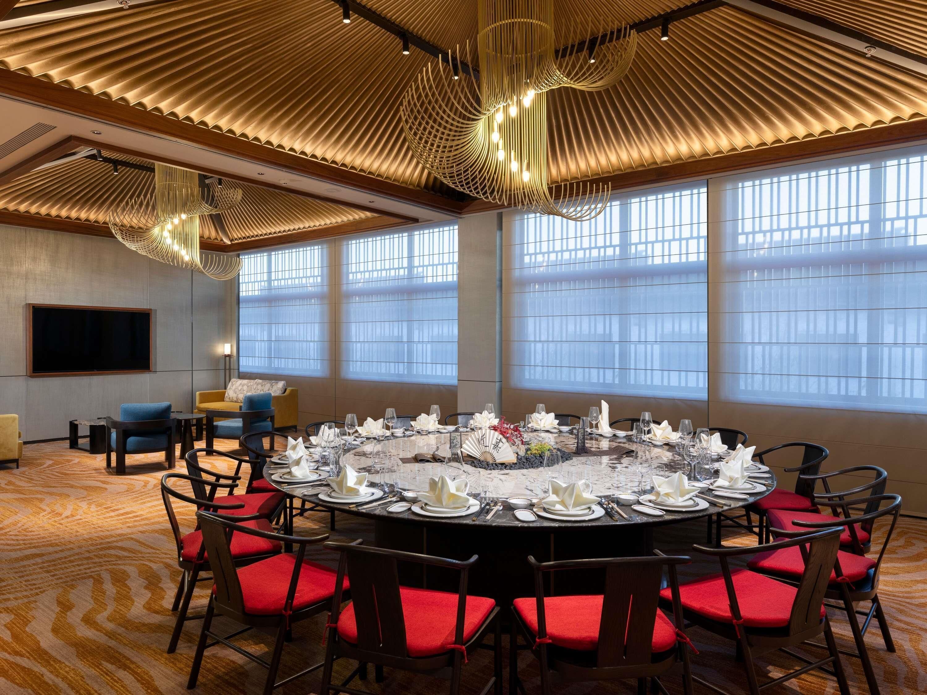A conference room with a round table set for a meeting, large windows, and a modern ceiling design.