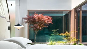 A modern room with a bed, a hanging lamp, and a view of a garden with plants and a tree. - Dangkou Ancient Town Hotel Wuxi - Mgallery Collection (Wuxi)