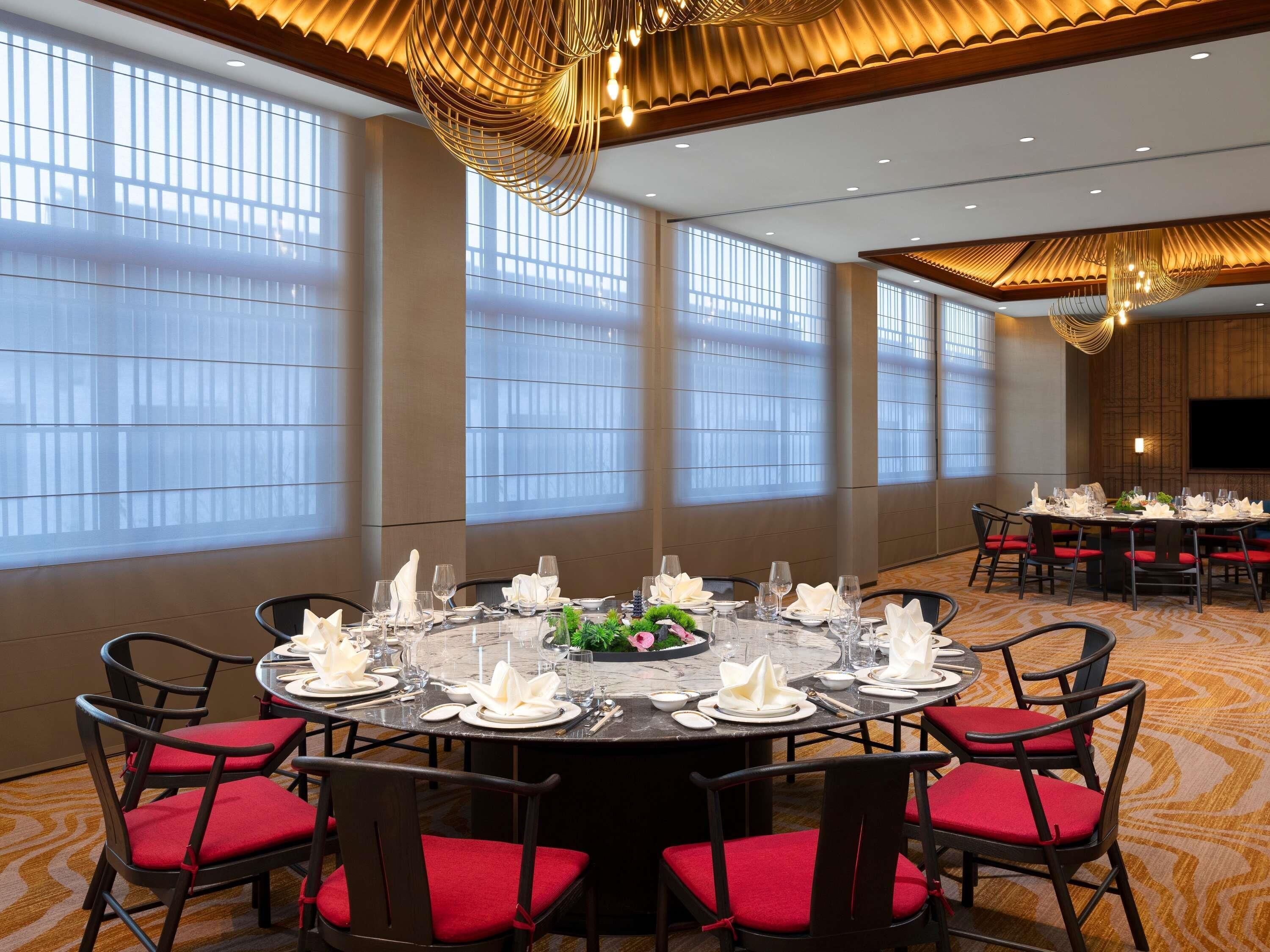 A conference room with a round table set for a meeting, equipped with chairs and a large screen.