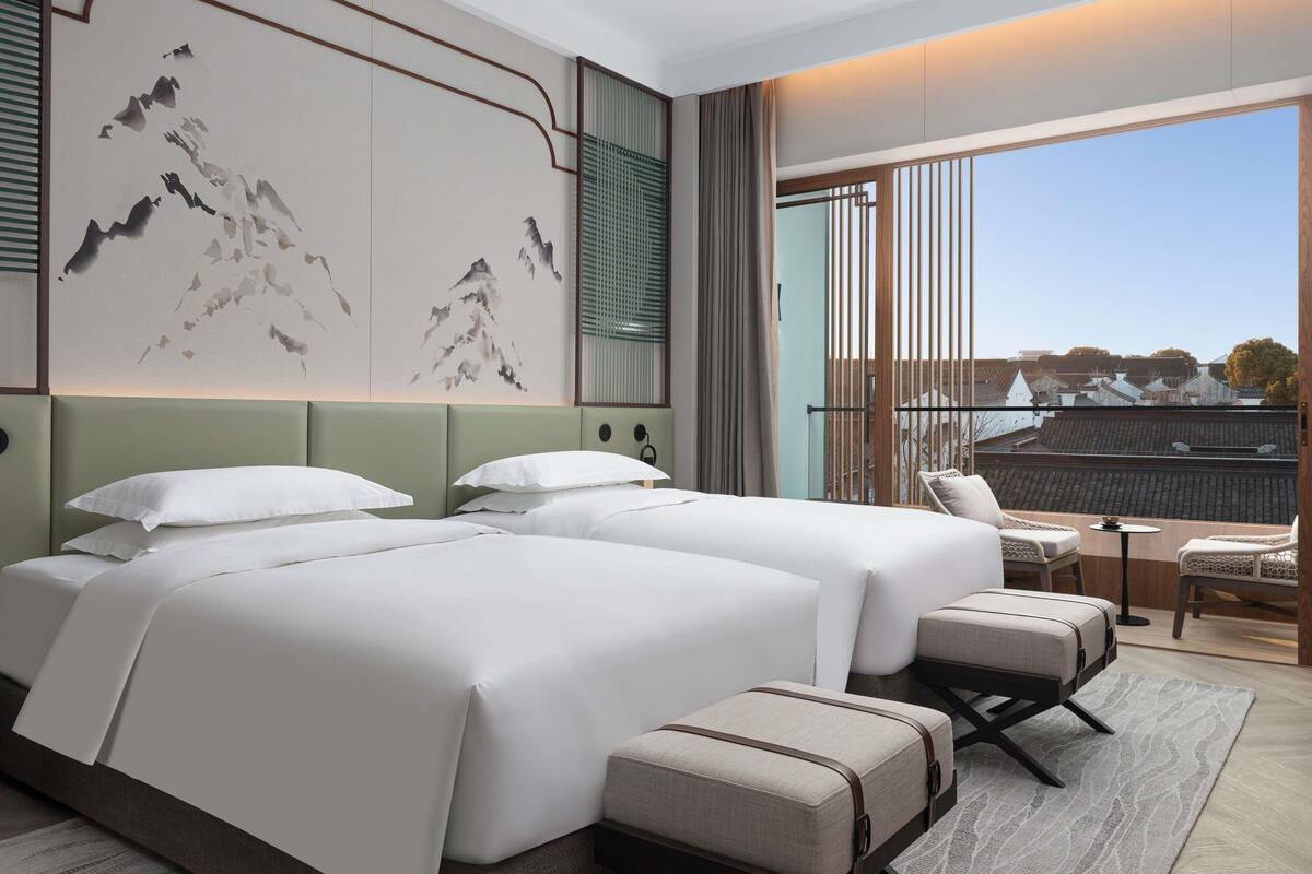 Habitación de hotel con dos camas, zona de estar y un amplio ventanal con vistas.