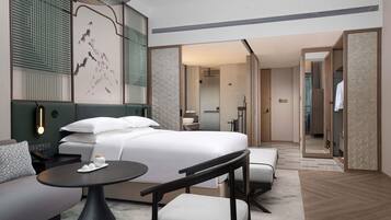 Una habitación de hotel moderna con una cama grande, una zona de estar con una mesa y sillas, un espejo y un vestidor.