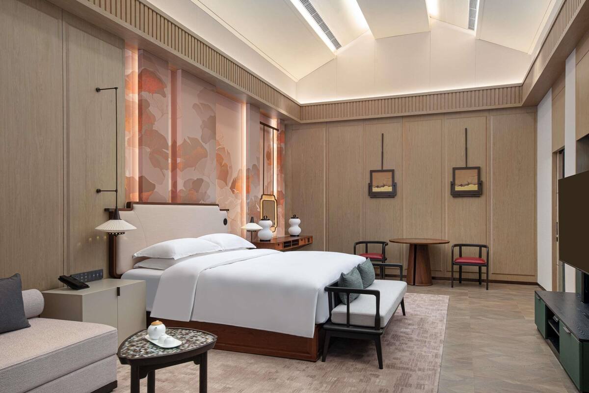 Una habitación de hotel con cama, mesita de noche, lámpara, silla y un mueble para televisor.