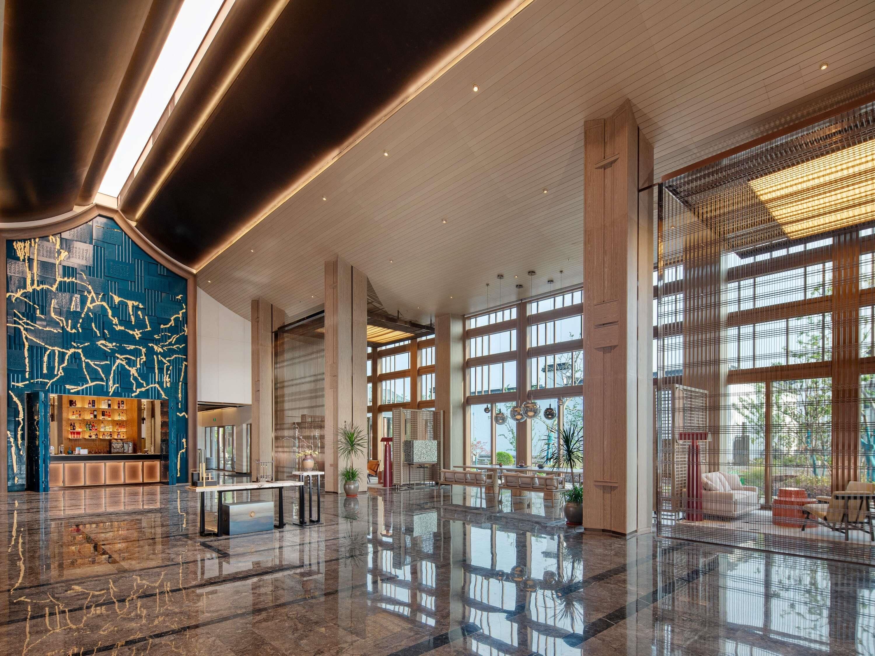 A spacious lobby with a high ceiling, large windows, and a polished marble floor.