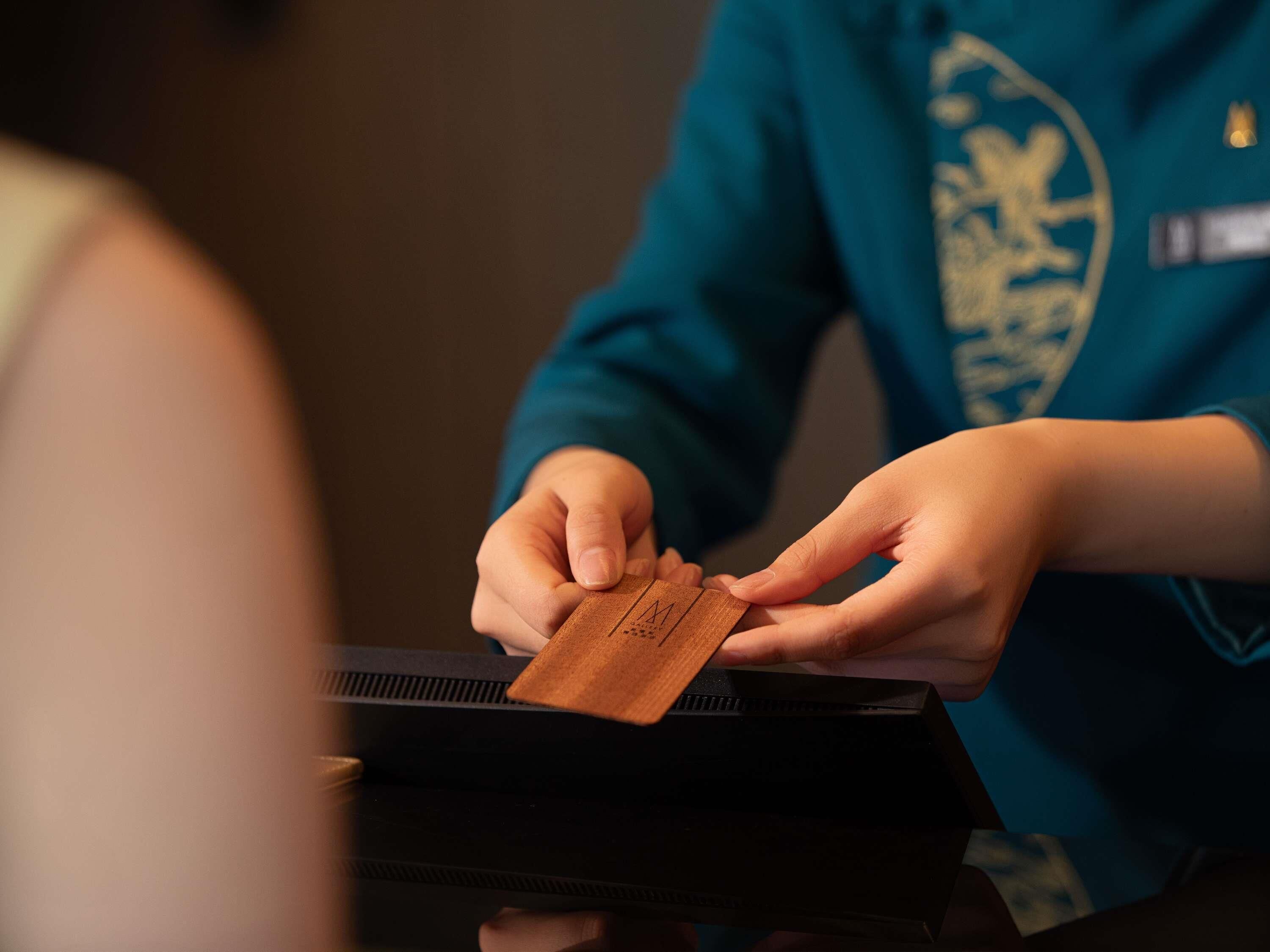Une personne tenant une carte avec un logo, debout à côté d’un appareil électronique noir.