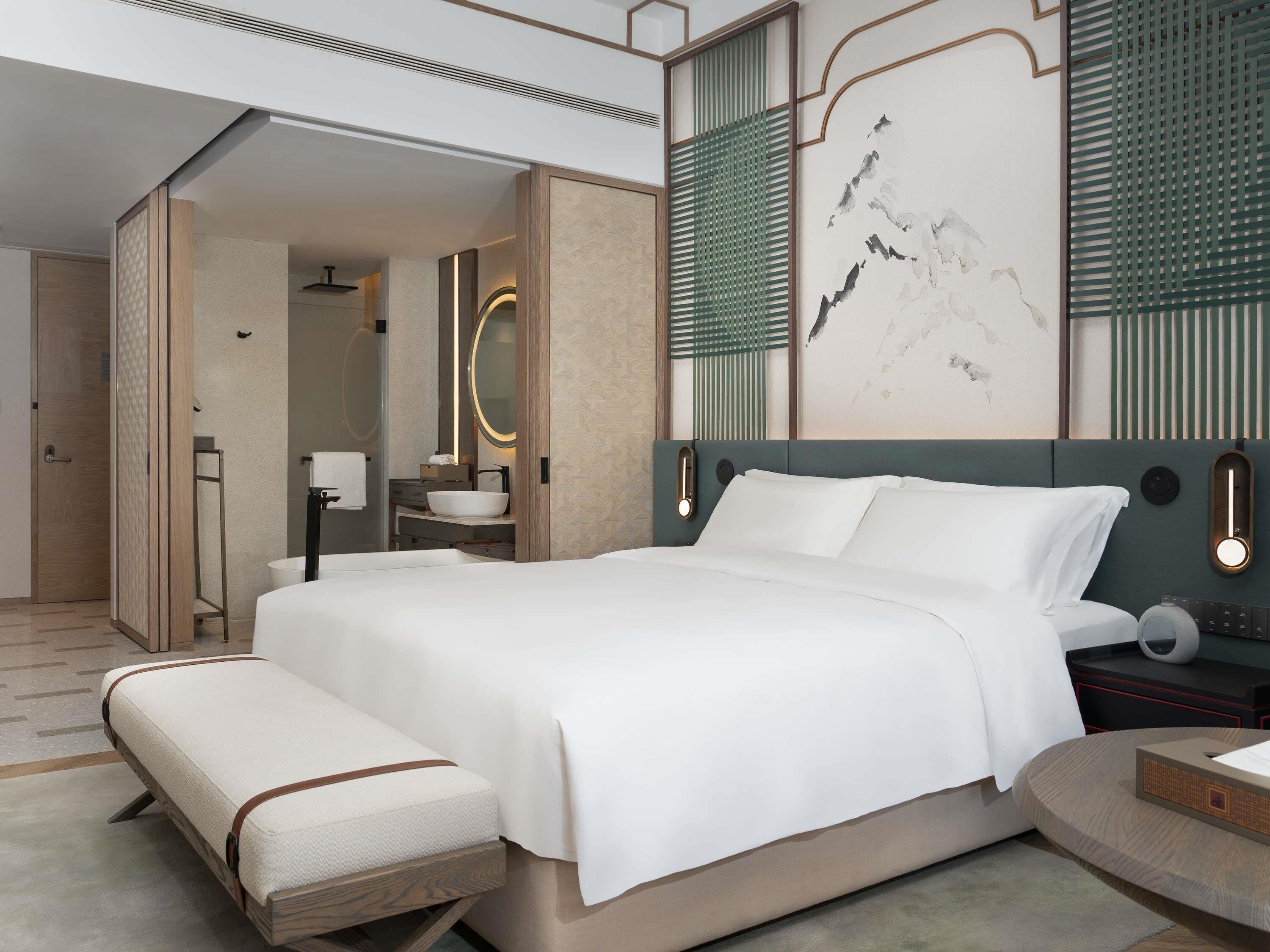 A modern bedroom with a large bed, bedside tables, a mirror, and a wall-mounted light fixture.