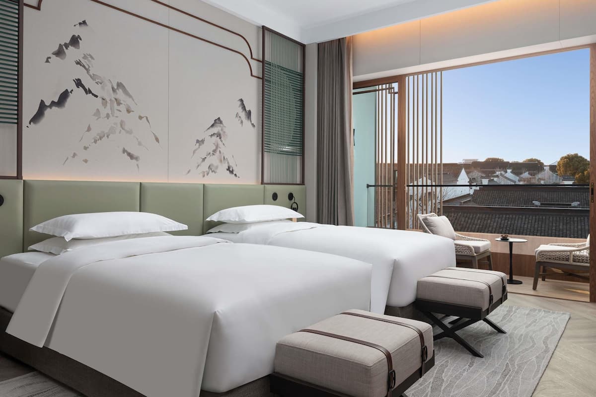 Een hotelkamer met twee bedden, een zithoek en een groot raam met uitzicht.