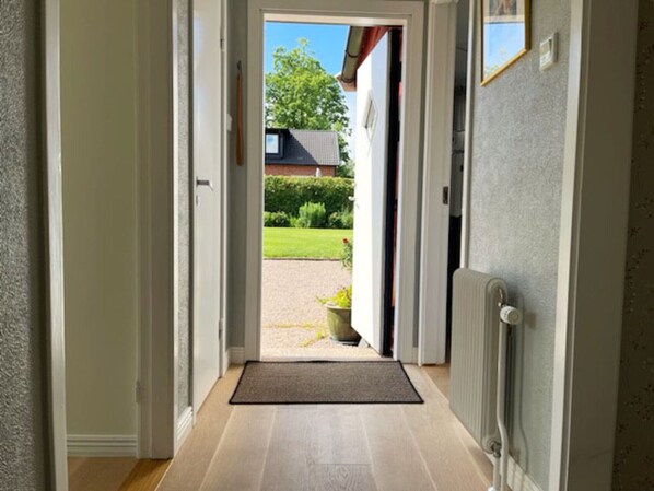 A hallway leading to a door with a view of a garden and a house.