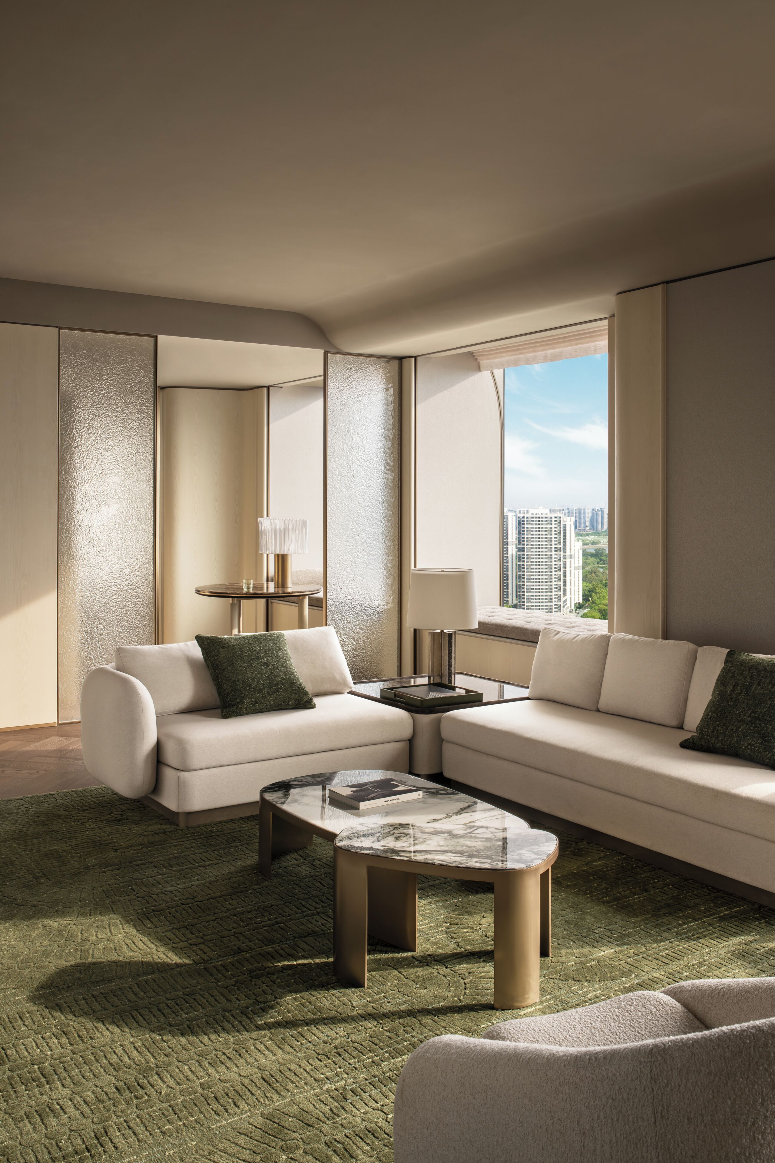 A modern living room with a sectional sofa, a round coffee table, and a view of the city through large windows.