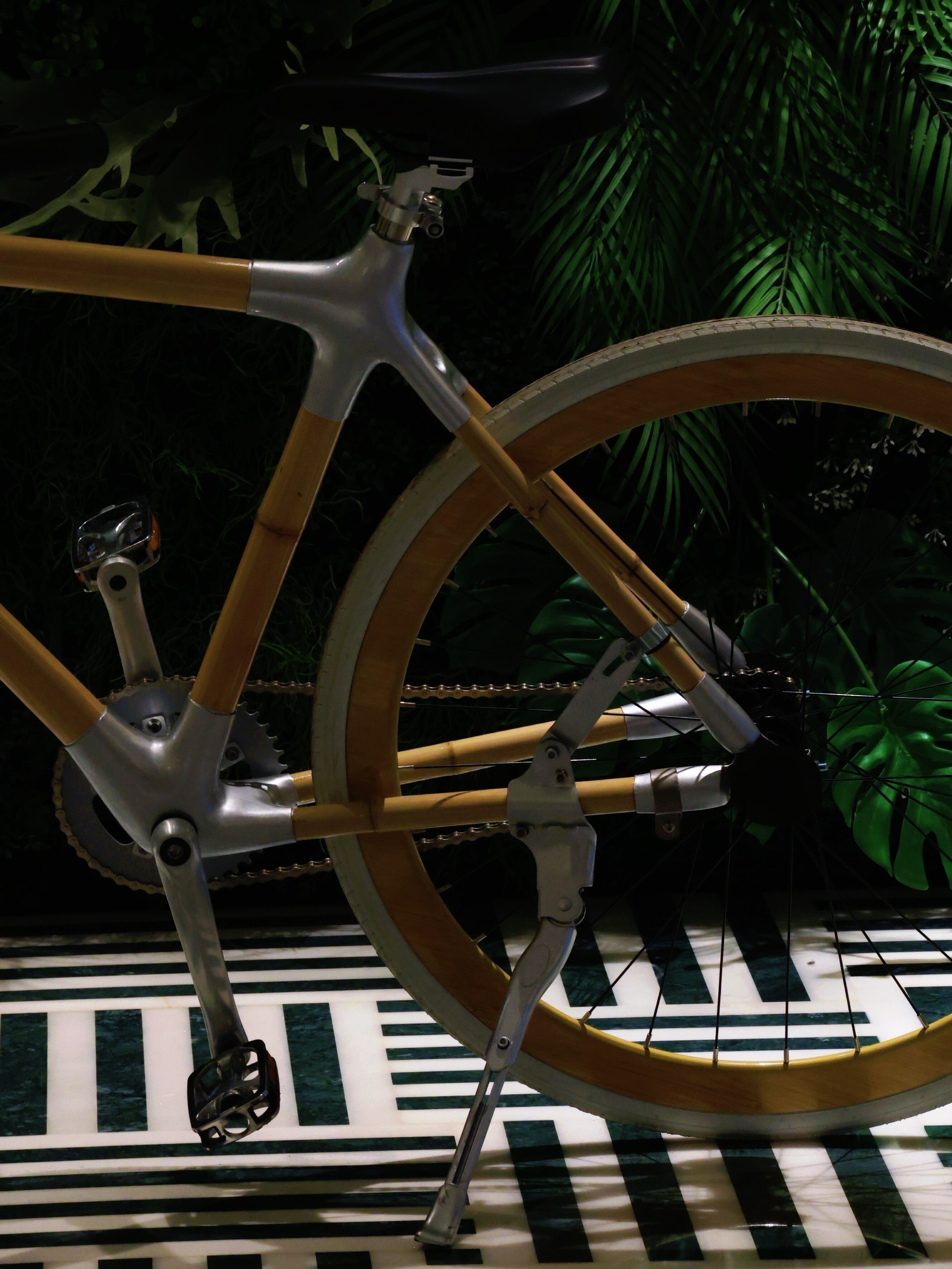 Una bicicleta amb estructura metàl·lica i components de fusta, sobre un terra amb dibuixos.