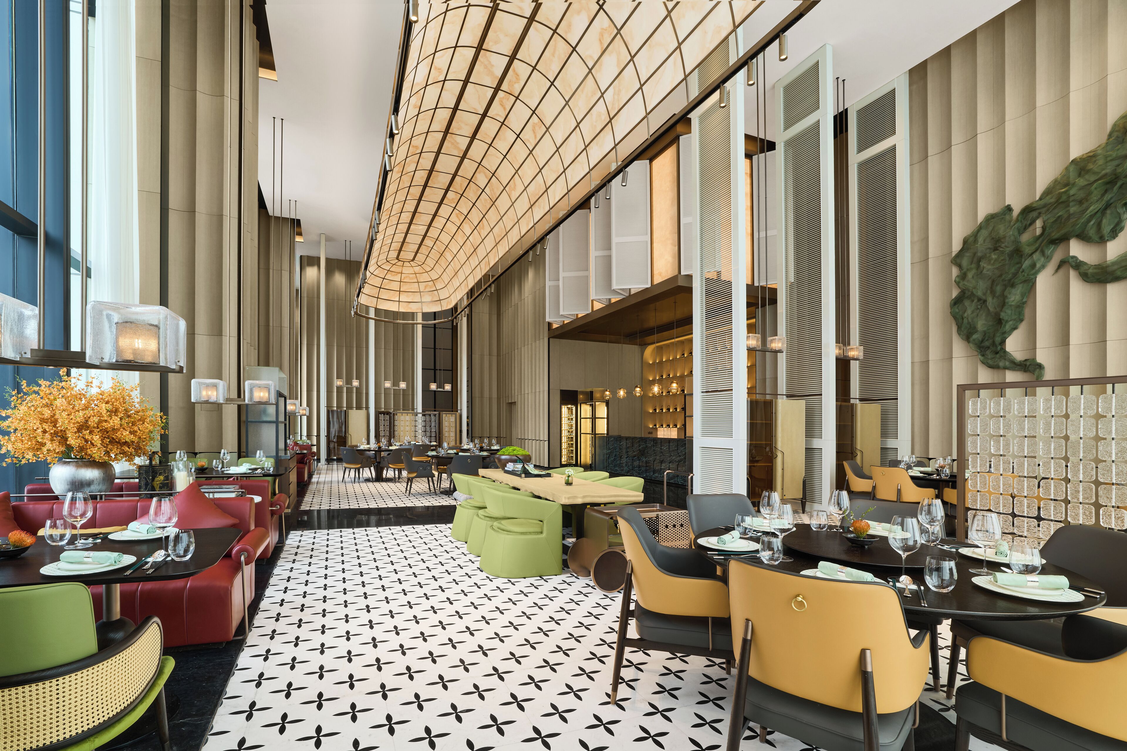 Ein modernes Restaurant mit einem schwarz-weiß gemusterten Boden, roten und grünen Sitzgelegenheiten und einer großen, grünen Wanddekoration.