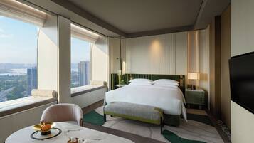 Habitación de hotel con una cama grande, una mesita de noche, una silla, vistas a la ciudad y un televisor.