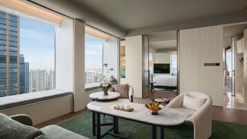 Quarto de hotel moderno com vista para a cidade, área de estar com mesa e quarto separado com cama e televisão.
