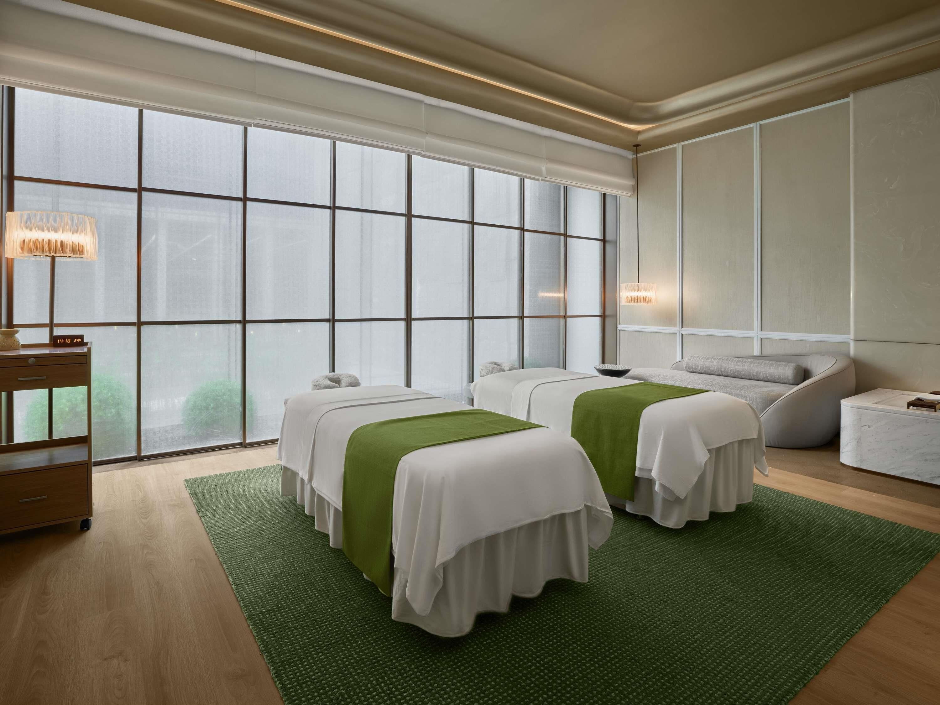 A hotel room with two beds, a desk, and a large window.